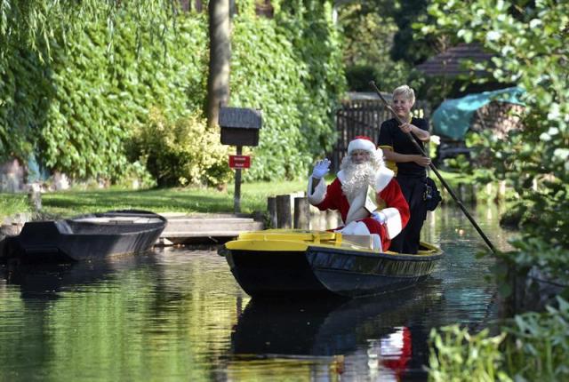 La cartera del servicio de correos alemán Andrea Bunar, que reparte el correo en una barca tradicional, lleva a Santa Claus durante su viaje de verano tradicional mientras busca regalos en un canal en Lehde (Alemania), hoy, martes 19 de agosto de 2014. La oficina de correos de navidades Himmelpfort celebra su 30 aniversario este año. EFE/Patrick Pleul