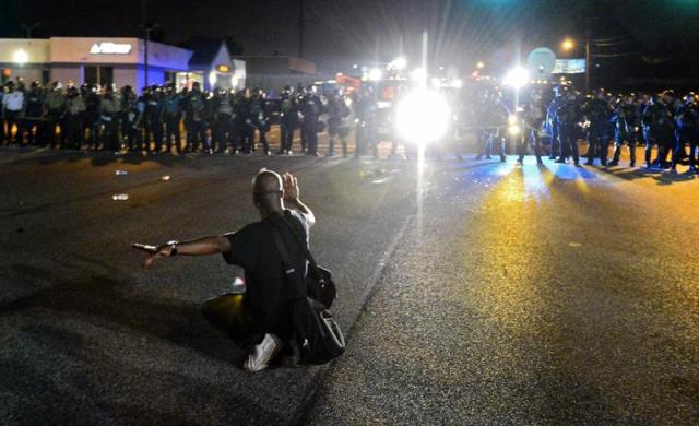 Agentes de la Policía vigilan las protestas en contra de la muerte del joven Michael Brown en Ferguson (Estados Unidos) ayer, lunes 18 de agosto de 2014. El gobernador del Estado de Misuri, en el medio oeste de EE.UU., Jay Nixon, movilizó a la Guardia Nacional ante los continuos disturbios tras la muerte de un joven negro desarmado en la localidad de Ferguson por un policía blanco que, según datos de una autopsia divulgados, le disparó seis veces. La orden del gobernador, que ya había relevado a la Policía local cuando fue reemplazada por la Patrulla de Carreteras estatal, asegura que la medida pretende restablecer la paz y el orden, así como proteger a los ciudadanos de Ferguson. EFE/Larry W. Smith