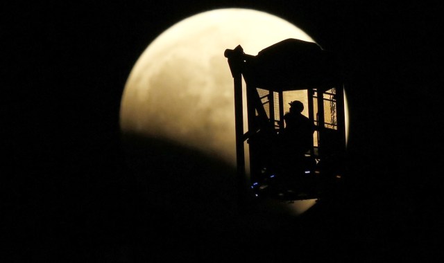 A man and a woman look at the moon as they ride a Ferris wheel, while a total lunar eclipse begins in Tokyo