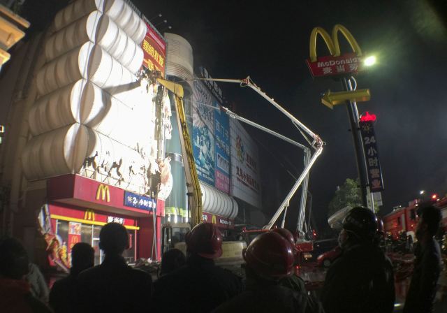 Firefighters break the exterior wall to clear the smoke inside the building after a fire broke out at a wholesale market building in Huidong county