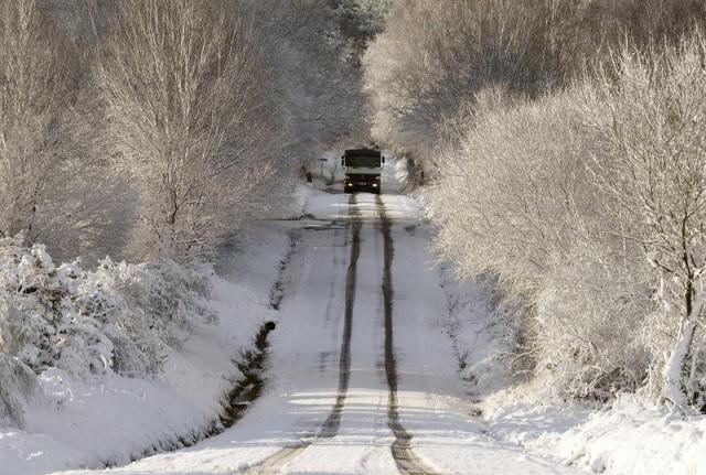 Un camión circula por una carretera nevada cerca de Monterroso, en la provincia de Lugo. La nieve, que esta mañana incluso se dejó ver en la capital lucense, está complicando la circulación por la red viaria de la provincia, especialmente en las carreteras provinciales y en las autonómicas, donde es preciso el uso de cadenas en al menos tres puertos de montaña. EFE/Eliseo Trigo