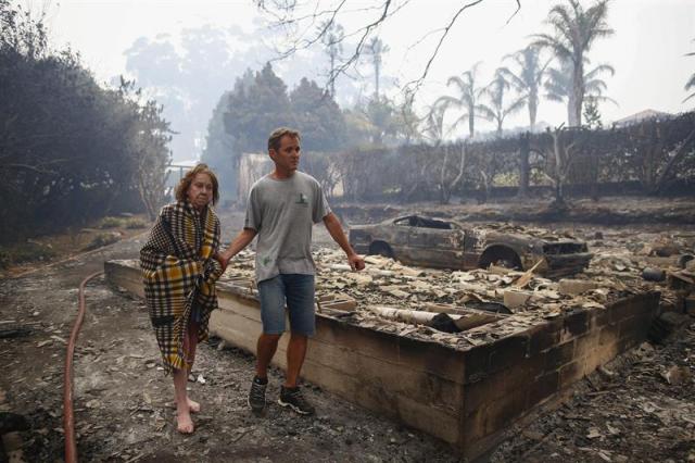 Un vecino ayuda a Fran Collings mientras camina entre los restos de su casa en Tokai en Ciudad del Cabo (Sudáfrica) hoy, miércoles 4 de marzo de 2015. Un incendio, que lleva activo cuatro días, ya ha arrasado más de 3.000 hectáreas en Ciudad del Cabo. EFE/Nic Bothma