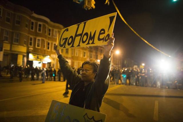 Una mujer muestra una pancarta en la que se puede leer "Iros a casa" durante una protesta contra la muerte de Freddie Gray en Baltimore (Estados Unidos) ayer, martes 28 de abril de 2015. La ciudad de Baltimore volvió a vivir este martes enfrentamientos violentos entre la Policía y manifestantes, que protestan por la muerte del joven negro, tras el inicio del toque de queda decretado por el Ayuntamiento desde las 22.00 hora local (02.00 GMT del miércoles). Dos mil miembros de la Guardia Nacional y otros mil policías patrullan las calles de Baltimore para tratar de evitar que se repitan los violentos sucesos del lunes que se saldaron con varios agentes heridos y numerosos daños materiales. EFE/John Taggart