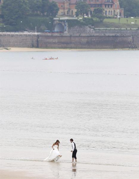 Una pareja de recién casados juega en la orilla de la playa de La Concha de San Sebastián, aprovechando un paréntesis de precipitaciones en una jornada marcada por la lluvia.EFE/Javier Etxezarreta.