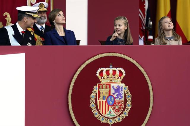 Los Reyes, acompañados por sus hijas, la Princesa Leonor y la infanta Sofía, que han presidido hoy el desfile del Día de la Fiesta Nacional, el último de esta legislatura, que ha durado una hora y diez minutos y en el que han participado 3.400 militares y guardias civiles, observan el paso de los aviones. EFE/Javier Lizon