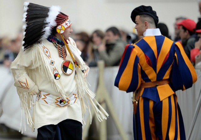 Un hombre nativo americano que lleva un traje tradicional camina pasar a un guardia suizo durante Francisco audiencia general en la plaza de San Pedro en el Vaticano el 27 de abril de 2016. FILIPPO MONTEFORTE / AFP