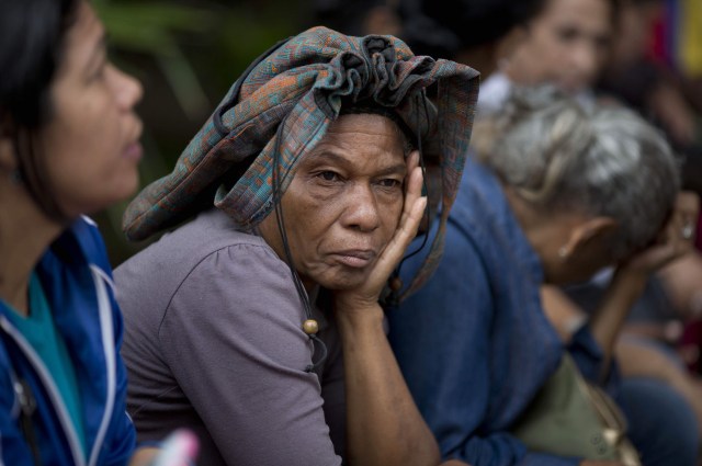 En esta fotografía del martes 3 de mayo de 2016, Adelaida Ospina se cubre la cabeza con un bolso de mano mientras espera en la fila afuera de un supermercado de Caracas, Venezuela, con el fin de comprar alimentos. El venezolano promedio pasa 35 horas al mes esperando para comprar productos básicos. Ospina dijo que llegó a las 5:40 de la mañana. (AP Foto/Ariana Cubillos)