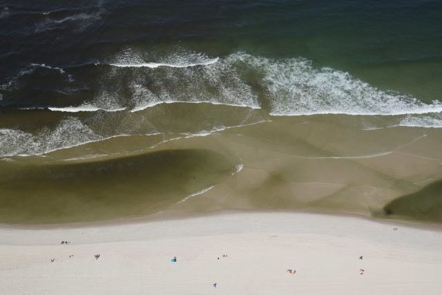 En esta foto del 5 de julio de 2016, una vista aérea muestra el agua contaminada, a la izquierda, que fluye desde el canal de la Barra hacia la playa de Barra en Río de Janeiro, Brasil. Es poco probable que los turistas se den cuenta de los peligros: en las playas había letreros que advertían sobre la calidad del agua, pero ya no están. Ahora un breve aviso en la página del clima del diario local enlista qué playas la agencia medioambiental del estado ha catalogado de seguras para nadar. (AP Foto/Felipe Dana)