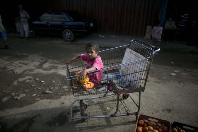 En esta imagen, tomada el 12 de septiembre de 2016, una niña espera sentada en un carro de supermercado mientras su padre trabaja en el mercado de Porlamar, en la isla de Margarita, en Venezuela. El padre de la niña, Alexander Velásquez, pasó la tarde pidiendo donaciones de comida a los vendedores del mercado Conejero, donde trabaja de portero. (AP Foto/Ariana Cubillos)