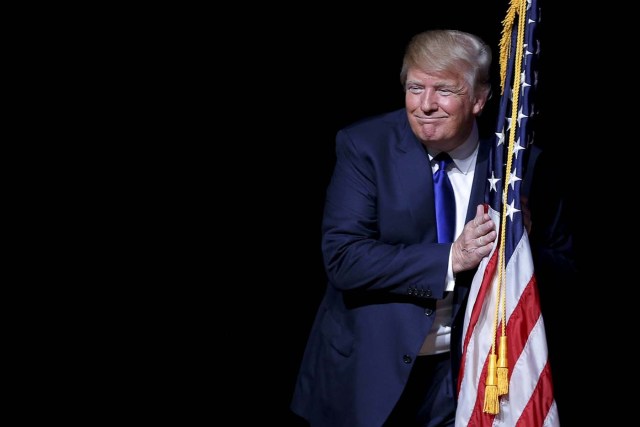 U.S. Republican presidential candidate Donald Trump hugs a U.S. flag as he takes the stage for a campaign town hall meeting in Derry, New Hampshire August 19, 2015. REUTERS/Brian Snyder /File Photo