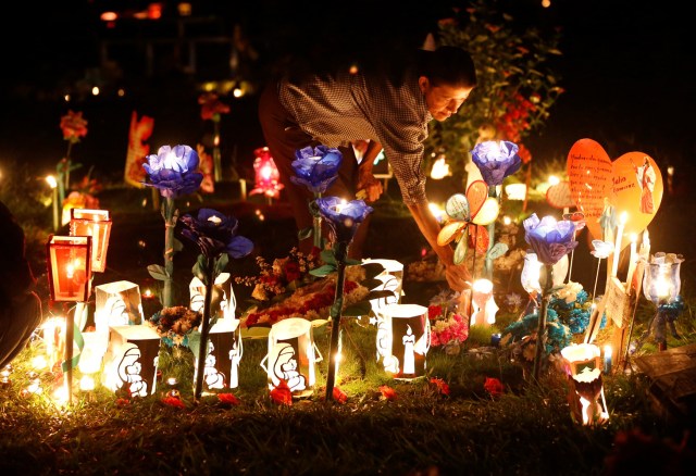 A woman lights candles, next to a grave in the cemetery "Jardines de la Aurora", to mark the beginning of the Christmas festivities, in Cali, Colombia, December 7, 2016. REUTERS/Jaime Saldarriaga