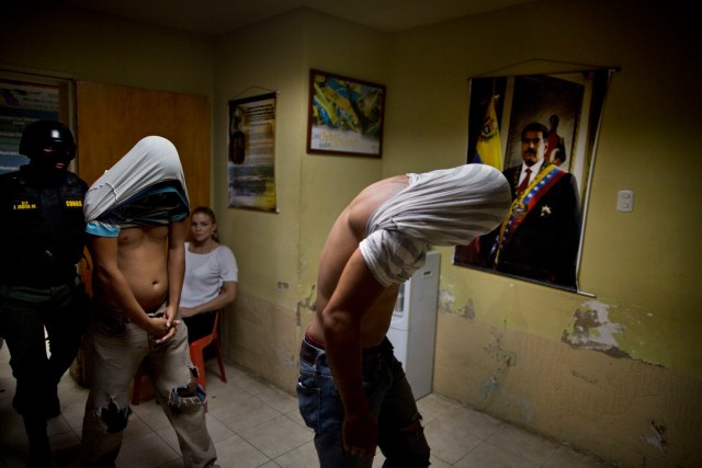 En esta foto del 5 de noviembre de 2016, hombres arrestados por supuestamente robar una motocicleta son escoltados por un oficial del comando antisecuestro y contra la extorsión de la Guardia Nacional en el centro de Cumaná, estado de Sucre, Venezuela. En el otoño, unos pandilleros decapitaron a un hombre y metieron la cabeza en su propio estómago. Semanas después, los miembros de una unidad militar de élite hincaron a nueve hombres frente a su casa y los mataron a tiros. (AP Foto/Rodrigo Abd)