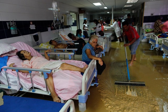 En esta foto del 3 de noviembre de 2016, un familiar de un paciente en el hospital público ayuda a sacar el agua de la sala de emergencias después de una fuerte lluvia que inundó el lugar en Cumaná, estado de Sucre, Venezuela. En el hospital faltan medicinas y camas. Algunos pacientes que van a los servicios de emergencia llegan a contraer infecciones bacterianas. (AP Foto/Rodrigo Abd)