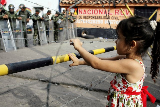 A girl stands next to a barbed wire fence as she waits to try to cross the border to Colombia over the Francisco de Paula Santander international bridge in Urena, Venezuela