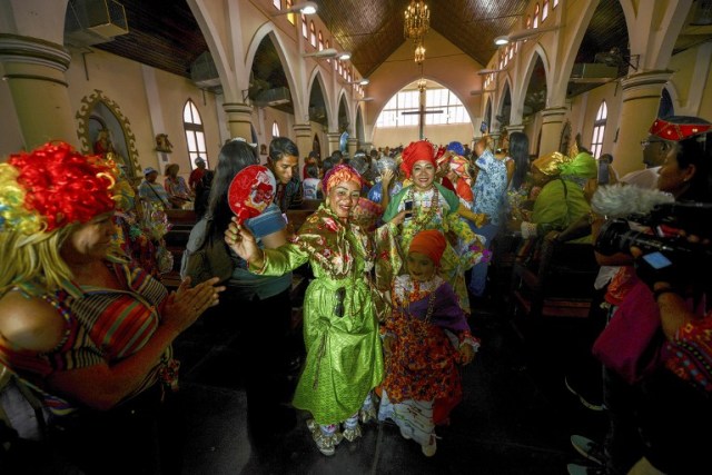 Women dressed as "madamas" attend a mass before the beginning of the Carnival in El Callao, Bolivar state, Venezuela on February 26, 2017. El Callao's carnival was recently named Unesco's Intangible Cultural Heritage of Humanity and is led by the madamas, the pillars of Callaoense identity representing Antillean matrons considered the communicators of values, who dance and wear colourful dresses. / AFP PHOTO / JUAN BARRETO