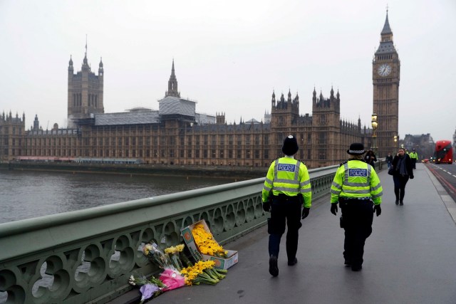 En la imagen, agentes de policía pasan por delante de ofrendas florales situadas en la escena del ataque en Westminster Bridge, en Londres, 24 de marzo de 2017. La policía británica dijo que realizó dos nuevos arrestos de carácter significativo en la investigación del ataque en el Parlamento de Londres y reveló el nombre de nacimiento del presunto autor, que se llamaría Adrian Russell Ajao. REUTERS/Darren Staples