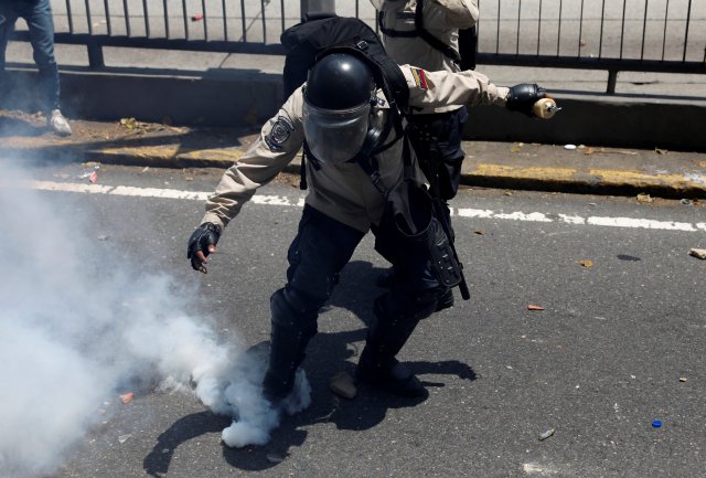 A riot police officer attempts to kick a gas canister during clashes with opposition supporters in Caracas, Venezuela