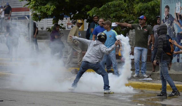 An opposition activist throws back tear gas during a march against President Nicolas Maduro, in Caracas on May 1, 2017. Security forces in riot vans blocked off central Caracas Monday as Venezuela braced for pro- and anti-government May Day protests one month after a wave of deadly political unrest erupted.  / AFP PHOTO / FEDERICO PARRA