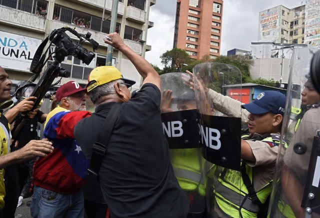 Opposition activists confront riot police during a protest against the government in Caracas on May 12, 2017. Daily clashes between demonstrators -who blame elected President Nicolas Maduro for an economic crisis that has caused food shortage- and security forces have left 38 people dead since April 1. Protesters demand early elections, accusing Maduro of repressing protesters and trying to install a dictatorship. / AFP PHOTO / JUAN BARRETO