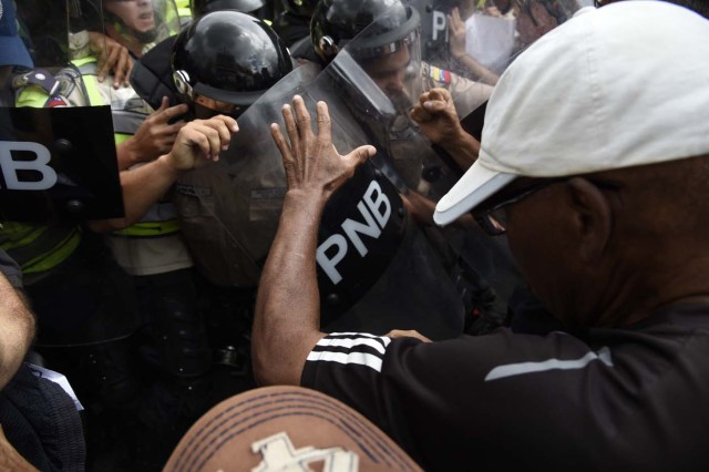 Opposition activists confront riot police during a protest against the government in Caracas on May 12, 2017. Daily clashes between demonstrators -who blame elected President Nicolas Maduro for an economic crisis that has caused food shortage- and security forces have left 38 people dead since April 1. Protesters demand early elections, accusing Maduro of repressing protesters and trying to install a dictatorship. / AFP PHOTO / JUAN BARRETO