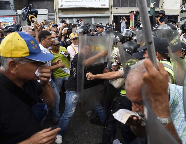 Opposition activists confront riot police during a protest against the government in Caracas on May 12, 2017. Daily clashes between demonstrators -who blame elected President Nicolas Maduro for an economic crisis that has caused food shortage- and security forces have left 38 people dead since April 1. Protesters demand early elections, accusing Maduro of repressing protesters and trying to install a dictatorship. / AFP PHOTO / JUAN BARRETO