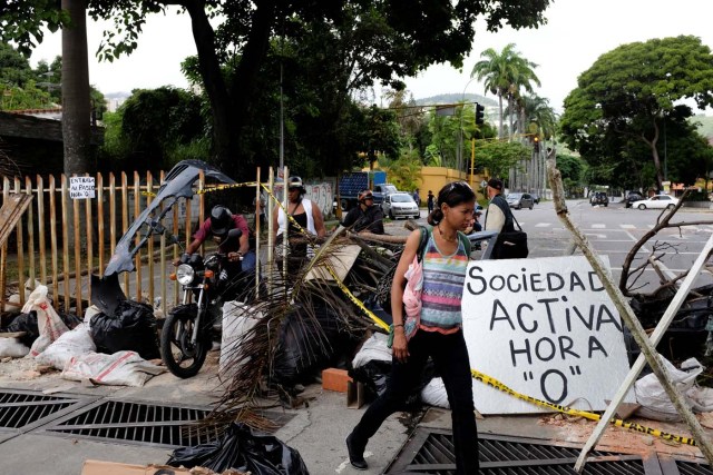 Pedestrians walk past a barricade during a rally against Venezuelan President Nicolas Maduro's government in Caracas, Venezuela July 19, 2017. The placard reads, "Active society. Hour 0". REUTERS/Marco Bello