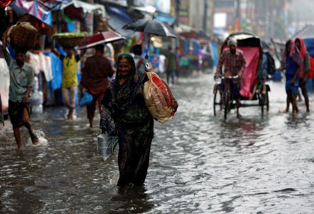 A woman with bags walks along a street as roads are flooded due to heavy rain in Dhaka, Bangladesh July 26, 2017. REUTERS/Mohammad Ponir Hossain