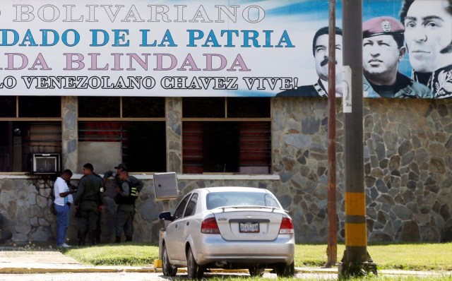 Members of security forces stand beneath a sign with portraits of Venezuela's President Nicolas Maduro, former President Hugo Chavez and Venezuela's national hero Simon Bolivar outside the 41 Brigada Blindada Fuerte Paramacay military base in Valencia, Venezuela August 6, 2017. REUTERS/Andres Martinez Casares