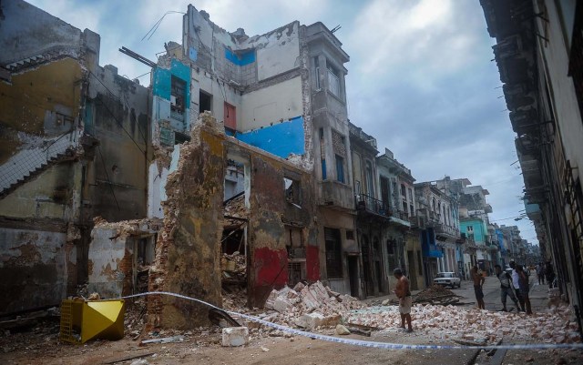 Cubans stand bt a collapsed building in Havana, on September 9, 2017. Irma's blast through the Cuban coastline weakened the storm to a Category Three, but it is still packing 125 mile-an-hour winds (205 kilometer per hour) and was expected to regain power before hitting the Florida Keys early Sunday, US forecasters said. The Cuban government extended its maximum state of alert to three additional provinces, including Havana, amid fears of flooding in low-lying areas. / AFP PHOTO / YAMIL LAGE