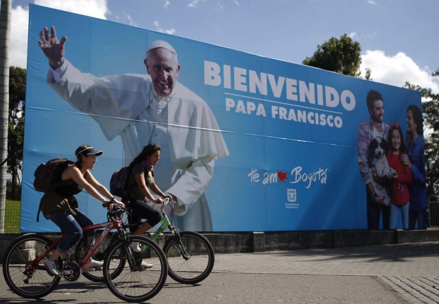 BOG508. BOGOTÁ (COLOMBIA), 06/09/2017.- Dos mujeres pasan en bicicleta frente a una pancarta con la imagen del papa Francisco hoy, miércoles 6 de septiembre de 2017, en Bogotá (Colombia). Centenares de policías y militares blindan hoy la avenida El Dorado, que lleva al aeropuerto internacional de Bogotá, para garantizar la seguridad durante el primer recorrido en papamóvil que hará el santo padre francisco tras su llegada esta tarde al país. EFE/LUIS EDUARDO NORIEGA A.