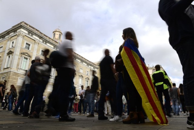 Una mujer envuelta con una bandera catalana de Estelada independentista se encuentra con otros en el Palacio de la Generalitat de Cataluña en Barcelona el 28 de octubre de 2017, un día después de que se impuso el control directo sobre la región en un intento por separarse de España. España se movió para afirmar el dominio directo sobre Cataluña, reemplazando a sus funcionarios ejecutivos y altos para sofocar un impulso de independencia que ha sumido al país en una crisis y ha puesto nerviosa a la Europa secesionista. / AFP PHOTO / PIERRE-PHILIPPE MARCOU