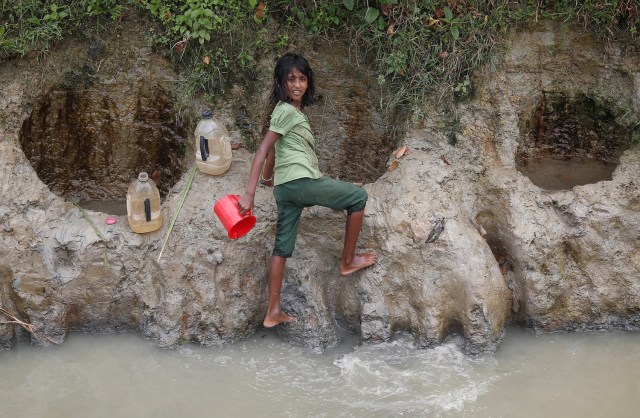 Una niña refugiada rohingya recoge agua de un pozo poco profundo, excavado en la arena a lo largo de un desagüe en el campo de refugiados de Uchiprang, cerca de Cox's Bazar, Bangladesh 29 de octubre de 2017. REUTERS / Adnan Abidi