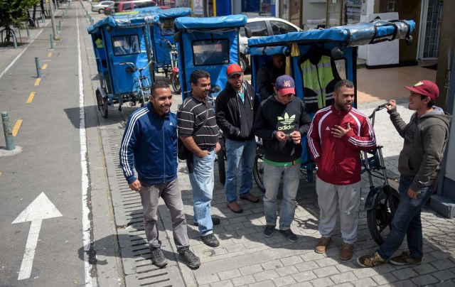 Venezuelan national Gregory Pacheco (L), 29, speaks with his compatriots before starting his working day as a "bicitaxi" (pedicab) driver in Bogota, on November 8, 2017. Up to October 2017 there were 470,000 Venezuelans in Colombia, who left their country to escape the hardship and violence of its economic and political crisis. / AFP PHOTO / Raul Arboleda / TO GO WITH AFP STORY by Daniela QUINTERO and Santiago TORRADO