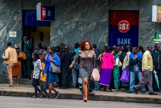 A woman passes the street as Harare residents queue outside a bank in Harare on November 15, 2017. Zimbabwe's military appeared to be in control of the country on November 15 as generals denied staging a coup but used state television to vow to target "criminals" close to President Mugabe. / AFP PHOTO / -