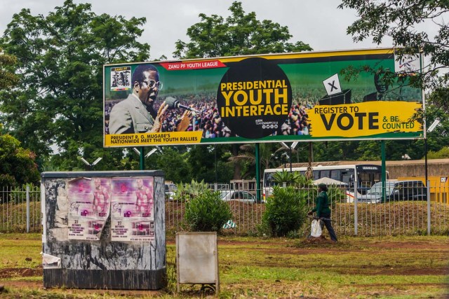 A woman in military uniform walks past a billboard with a poster of ruling party Zimbabwe African National Union - Patriotic Front (Zanu PF) and a picture of President Robert Mugabe in Harare on November 15, 2017. Zimbabwe's military appeared to be in control of the country on November 15 as generals denied staging a coup but used state television to vow to target "criminals" close to President Mugabe. / AFP PHOTO / -