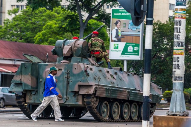 A man walks past an armoured personnel carrier that stations by an intersection as Zimbabwean soldiers regulate traffic in Harare on November 15, 2017. Zimbabwe's military appeared to be in control of the country on November 15 as generals denied staging a coup but used state television to vow to target "criminals" close to President Mugabe. / AFP PHOTO / -