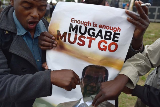 A man gestures towards a banner during a demonstration demanding the resignation of Zimbabwe's president on November 18, 2017 in Harare. Zimbabwe was set for more political turmoil November 18 with protests planned as veterans of the independence war, activists and ruling party leaders called publicly for President Robert Mugabe to be forced from office. / AFP PHOTO / -