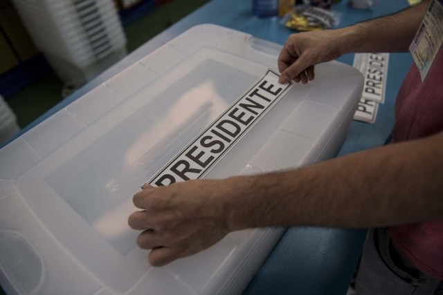 A man places a sticker reading "President" on a ballot box as polling stations are being set up at the National Stadium in Santiago on November 18, 2017 on the eve of Chile's general elections. After four years of socialist rule, Chile is expected to revert to the right in elections Sunday, with Sebastian Pinera set to return as president, confirming a shift to conservative leaders across Latin America. Opinion polls make Pinera, a 67-year-old billionaire businessman sometimes referred to as "Chile's Berlusconi", the hot favourite to return to the presidency he occupied from 2010-2014. / AFP PHOTO / Martin BERNETTI