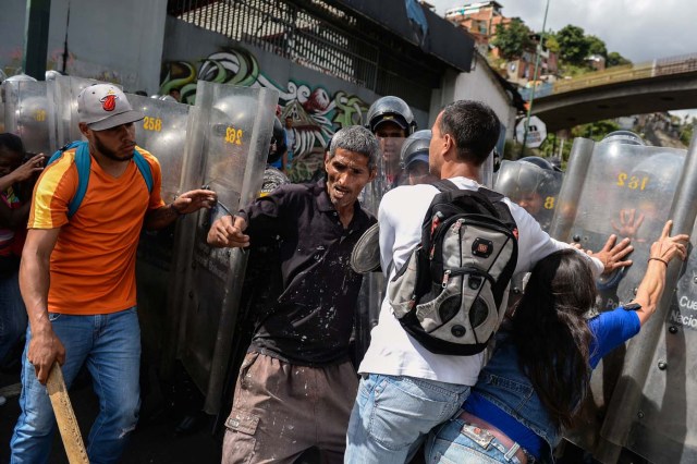 People confront riot police during a protest against the shortage of food, amid Fuerzas Armadas avenue in Caracas on December 28, 2017. As Venezuelans protest in Caracas demanding the government's prommised pork -the main dish of the Christmas and New Year's dinner-, President Nicolas Maduro attributes the shortage to international sabotage. / AFP PHOTO / FEDERICO PARRA