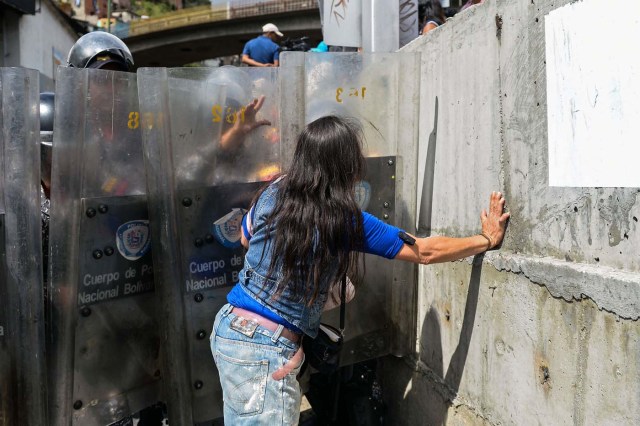 A woman confronts riot police during a protest against the shortage of food in Caracas on December 28, 2017. As Venezuelans protest in Caracas demanding the government's prommised pork -the main dish of the Christmas and New Year's dinner-, President Nicolas Maduro attributes the shortage to international sabotage. / AFP PHOTO / FEDERICO PARRA