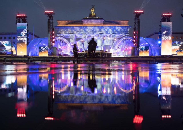 The stage and the illuminated Brandenburg Gate reflect in a puddle as preparations are under way for New Year's Eve celebrations in Berlin on December 30, 2017. / AFP PHOTO / DPA / Ralf Hirschberger / Germany OUT