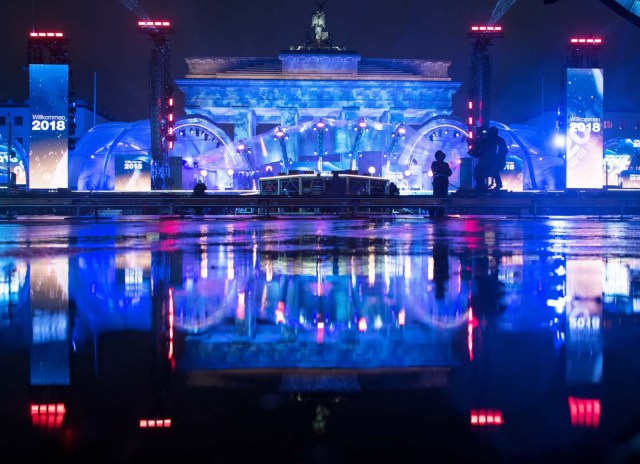 The stage and the illuminated Brandenburg Gate reflect in a puddle as preparations are under way for New Year's Eve celebrations in Berlin on December 30, 2017. / AFP PHOTO / DPA / Ralf Hirschberger / Germany OUT