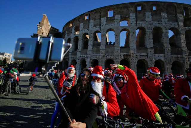 Cyclists dressed as Santa Claus pose for a tourist as they meet at the Colosseum in Rome, Italy December 17, 2017. REUTERS/Tony Gentile