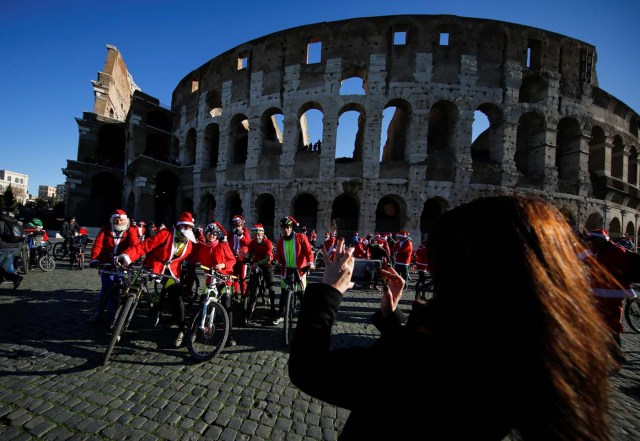 Cyclists dressed as Santa Claus pose for a tourist as they meet at the Colosseum in Rome, Italy December 17, 2017. REUTERS/Tony Gentile