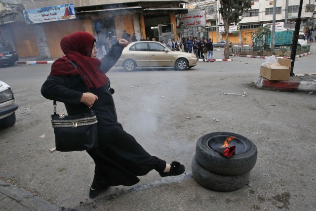 A Palestinian demonstrator kicks tyres during clashes with Israeli security forces near a checkpoint in the city centre of the West Bank town of Hebron on December 20, 2017. / AFP PHOTO / HAZEM BADER