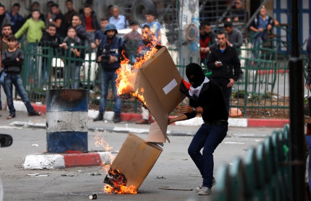 HEB18. HEBRÓN (PALESTINA), 20/12/2017.- Un palestino quema cajas de cartón mientras otros lanzan piedras a las tropas israelíes durante disturbios por la decisión del presidente estadounidense, Donald Trump, de reconocer Jerusalén como capital israelí, en Hebrón (Palestina) hoy, 20 de diciembre de 2017. EFE/ Abed Al Hashlamoun