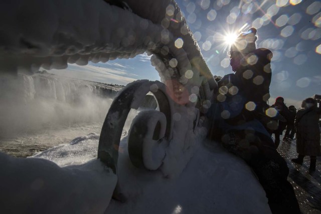 Tourists look at a nearly frozen Niagara Falls in Niagara Falls, Ontario on January 3, 2018. The cold snap which has gripped much of Canada and the United States has nearly frozen over the American side of the falls. / AFP PHOTO / Geoff Robins