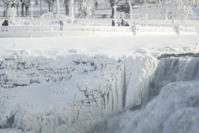 Tourists in Niagara Falls, New York, walk near the nearly frozen American side of Niagara Falls, January 3, 2018. The cold snap which has gripped much of Canada and the United States has nearly frozen over the American side of the falls. / AFP PHOTO / Geoff Robins