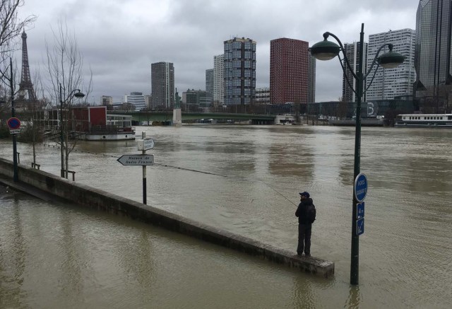 The Eiffel Tower (L) is seen in the background as a man fishes off a barrier partially submerged by the water of the swollen Seine river in Paris on January 28, 2018. The swollen Seine rose even higher on January 28, keeping Paris on alert, though forecasters said the flooding should peak by the end of the day. / AFP PHOTO / Stéphane DELFOUR