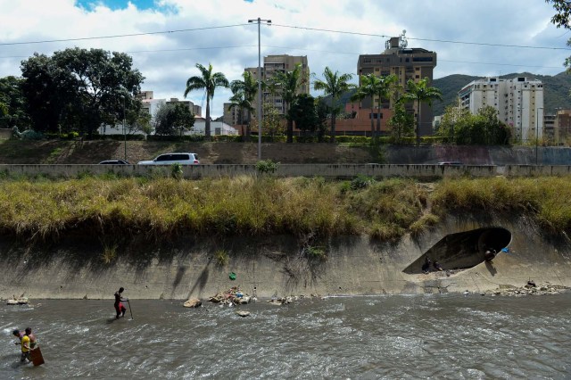 Los hombres buscan metales valiosos en un canal de aguas residuales en el río Guaire, en Caracas, el 1 de febrero de 2018. Decenas de jóvenes buscan diariamente joyas perdidas en el río Guaire, donde drenan las alcantarillas de Caracas. Encontrar oro es su ilusión, pero una pieza de alambre de cobre es suficiente para paliar el hambre. / AFP PHOTO / FEDERICO PARRA